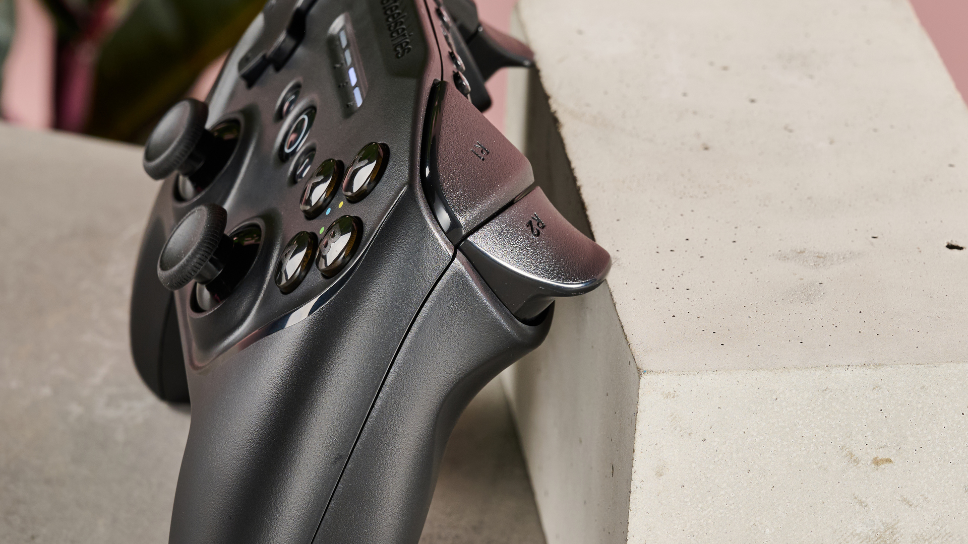 Side view of SteelSeries Stratus Duo leaning on plinth on table with pink wall and plant in background