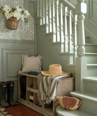 small hallway painted in soft green with small wooden storage unit acting as shoe store and foot bench