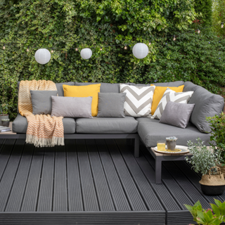 Black wooden decking with grey sofa cushions in front of hedge
