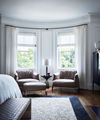 white bedroom with chairs in window and fluffy rug
