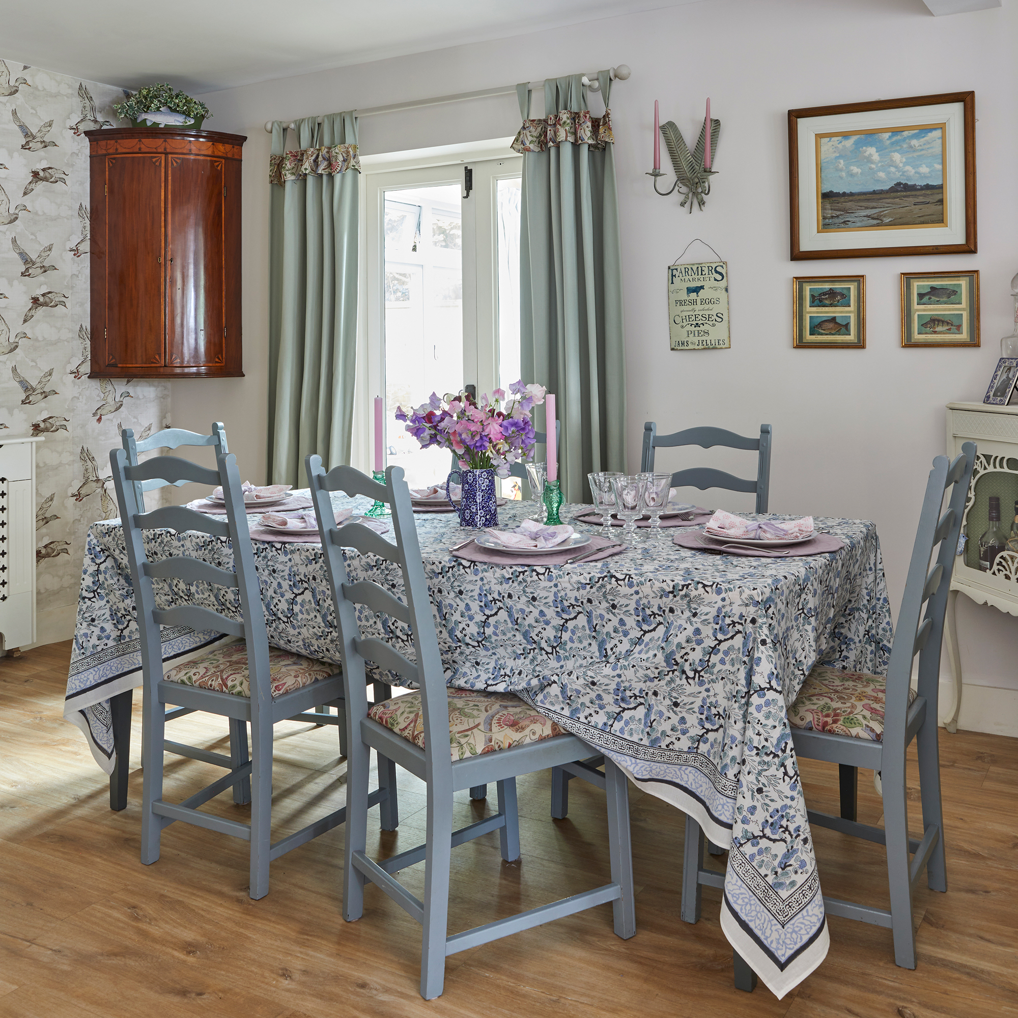country style dining room with feature wallpaper, blue painted traditional chairs and patterend tablecloth