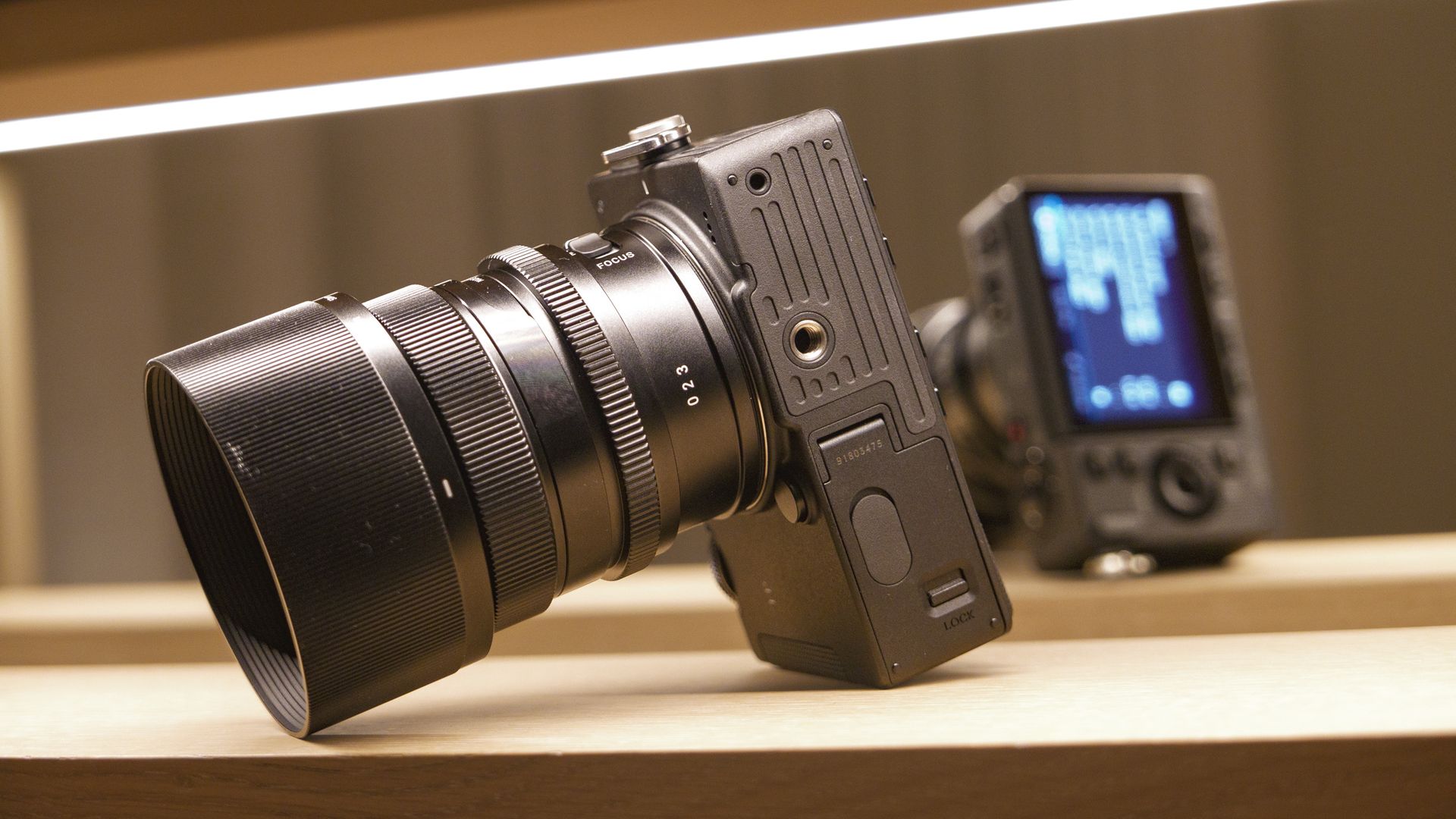 Sigma FP2 mirrorless camera with 50mm f/2 contemporary lenses attached, on a shelf, lit from above, close up of it's underside