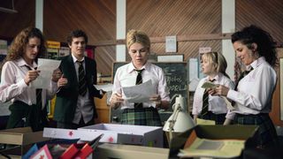 girls in catholic school uniforms look at papers in a school office in derry girls