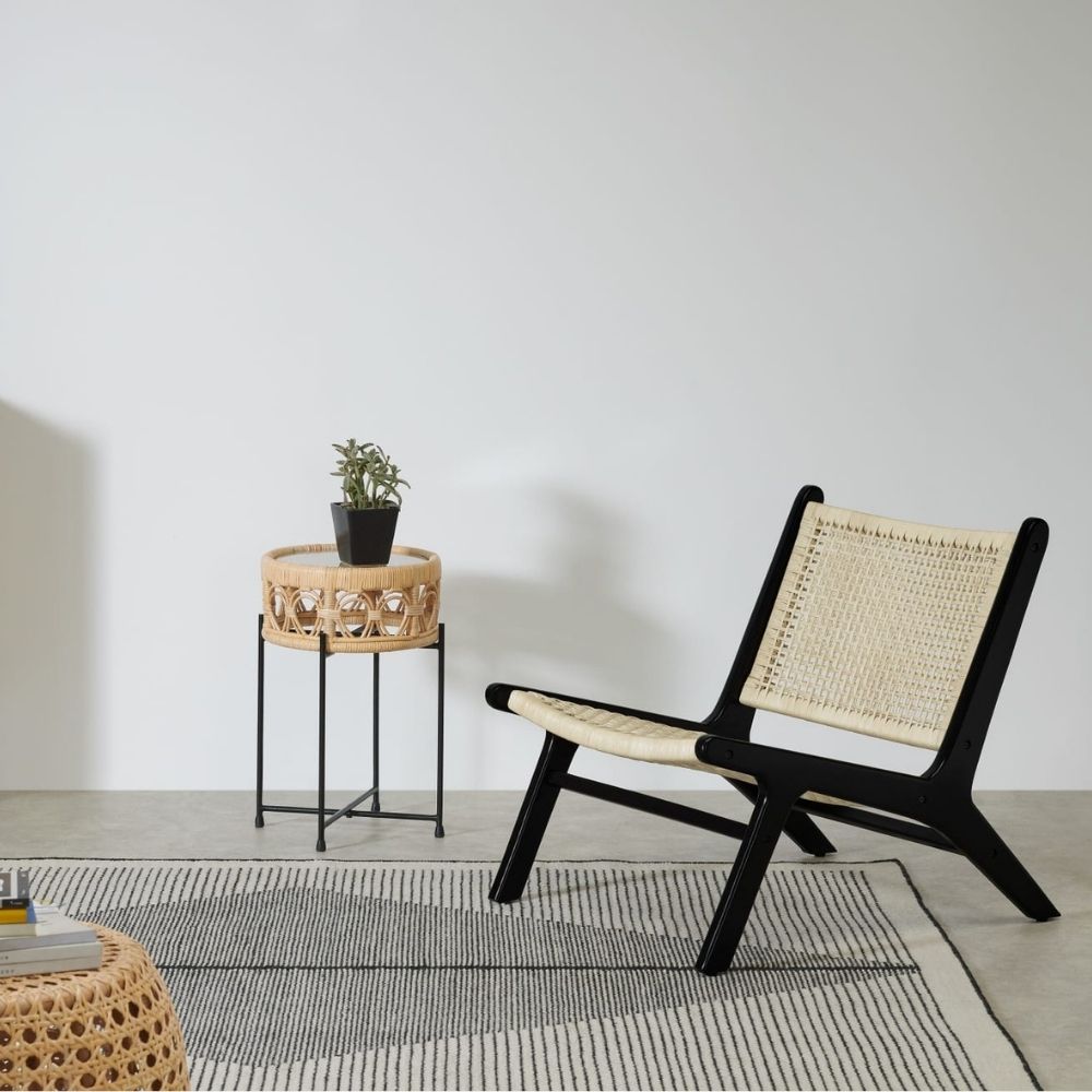 MADE Modica Accent Armchair, black frame with rattan seat and back, beside small side table and on top of black and white rug