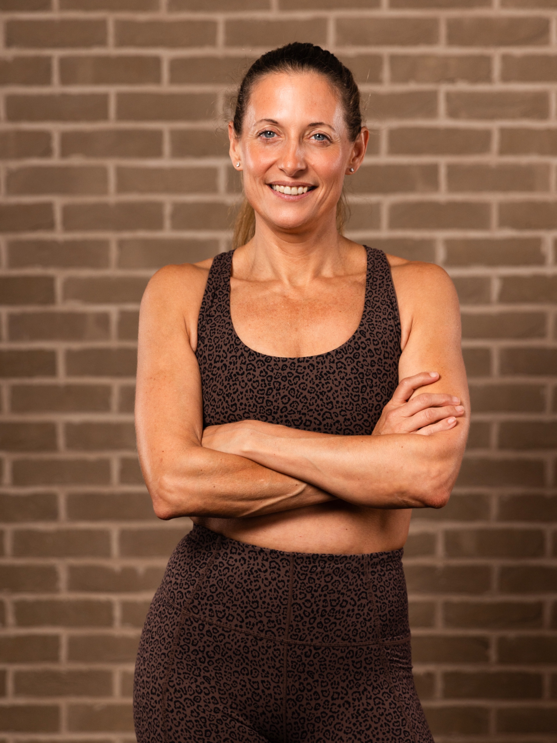 A woman with dark hair standing in sports bra and leggings with her arms crossed