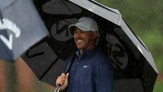 Brooks Koepka smiles under an umbrella during The Masters