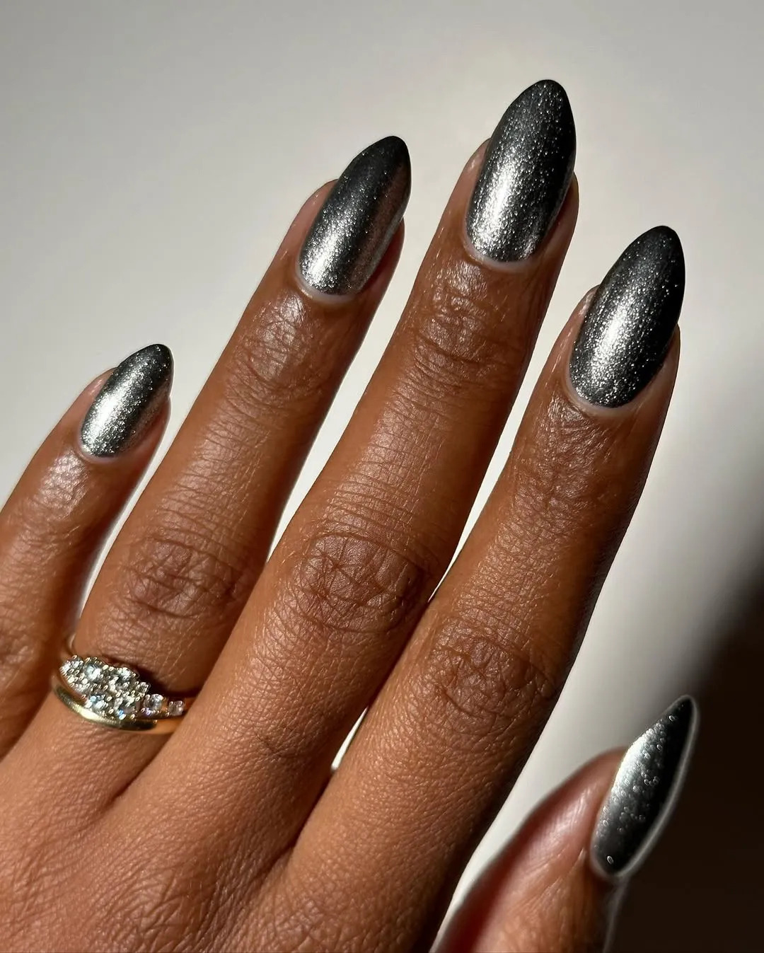 a close up of a silver metallic manicure on a woman's hand with a diamond ring