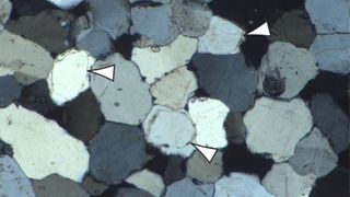 Microscope image from the sarsen sample showing the tightly interlocking mosaic of quartz crystals that cement the rock together. The outlines of quartz sand grains are indicated by arrows.