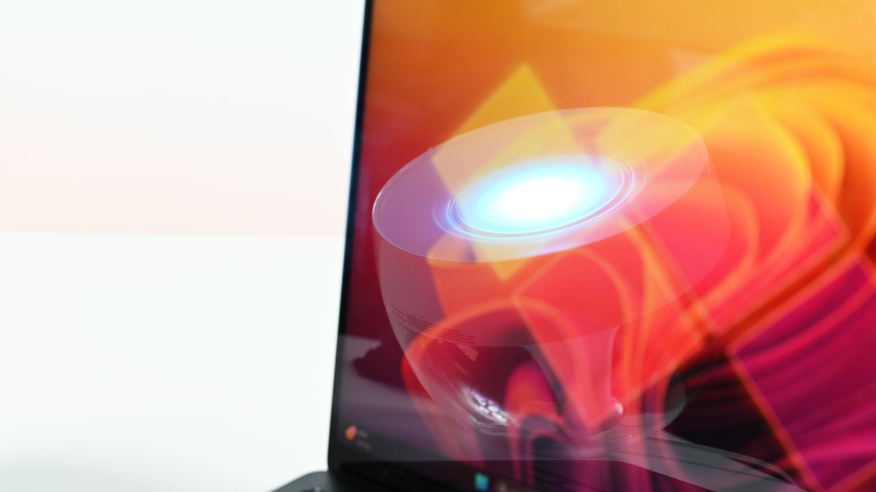 Close-up of a laptop screen displaying vibrant, abstract digital art. The artwork features swirling waves of orange and red, with a glowing blue circle.