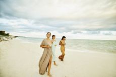 Wide shot of female friends walking on beach at tropical resort at sunset