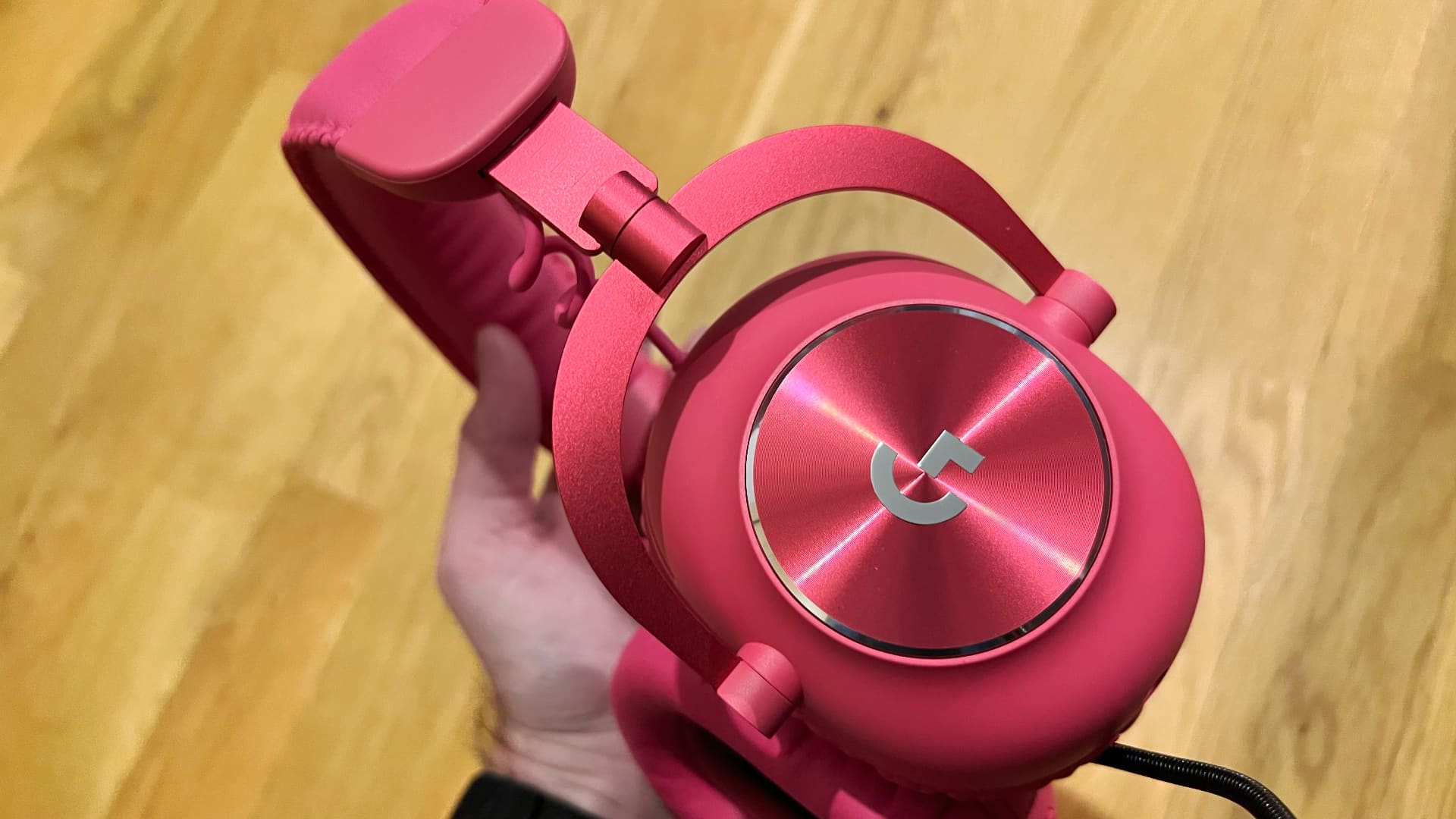 En hand håller upp ett par rosa Logitech G PRO X 2 LIGHTSPEED och visar upp ena öronkåpan.