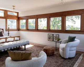 Traditional-style bedroom with wooden trim around window, wooden flooring, two cozy cream armchairs, rug, daybed and bed