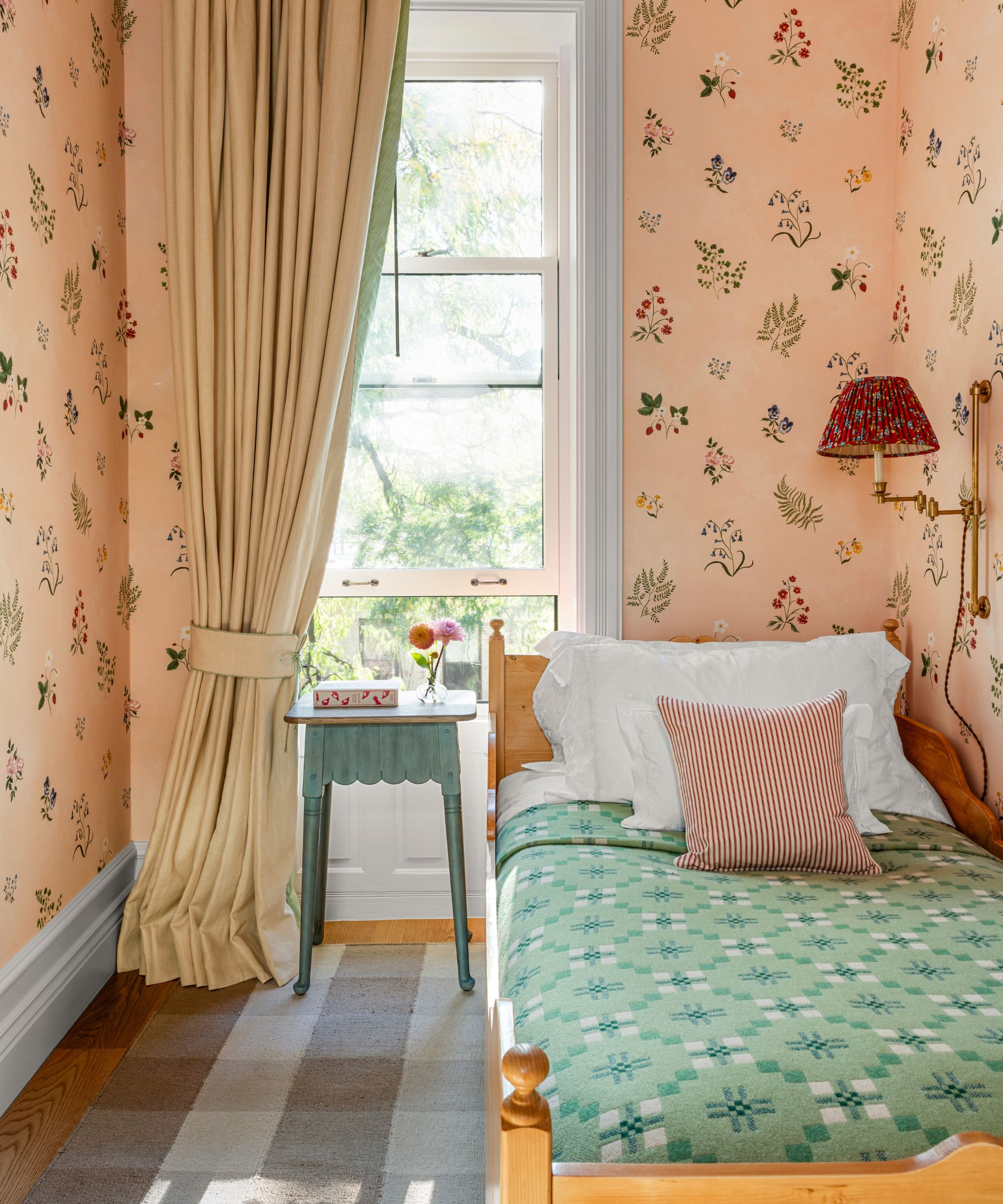 a small single guest bedroom wallpapered in pink floral paper with a small pine bed styled with white linens and a welsh blanket