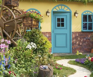 A beautiful flower garden in front of a yellow house with bright teal windows and door