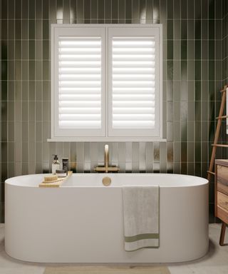 bathroom with narrow green wall tiles, white shutters over window and white modern freestanding bath