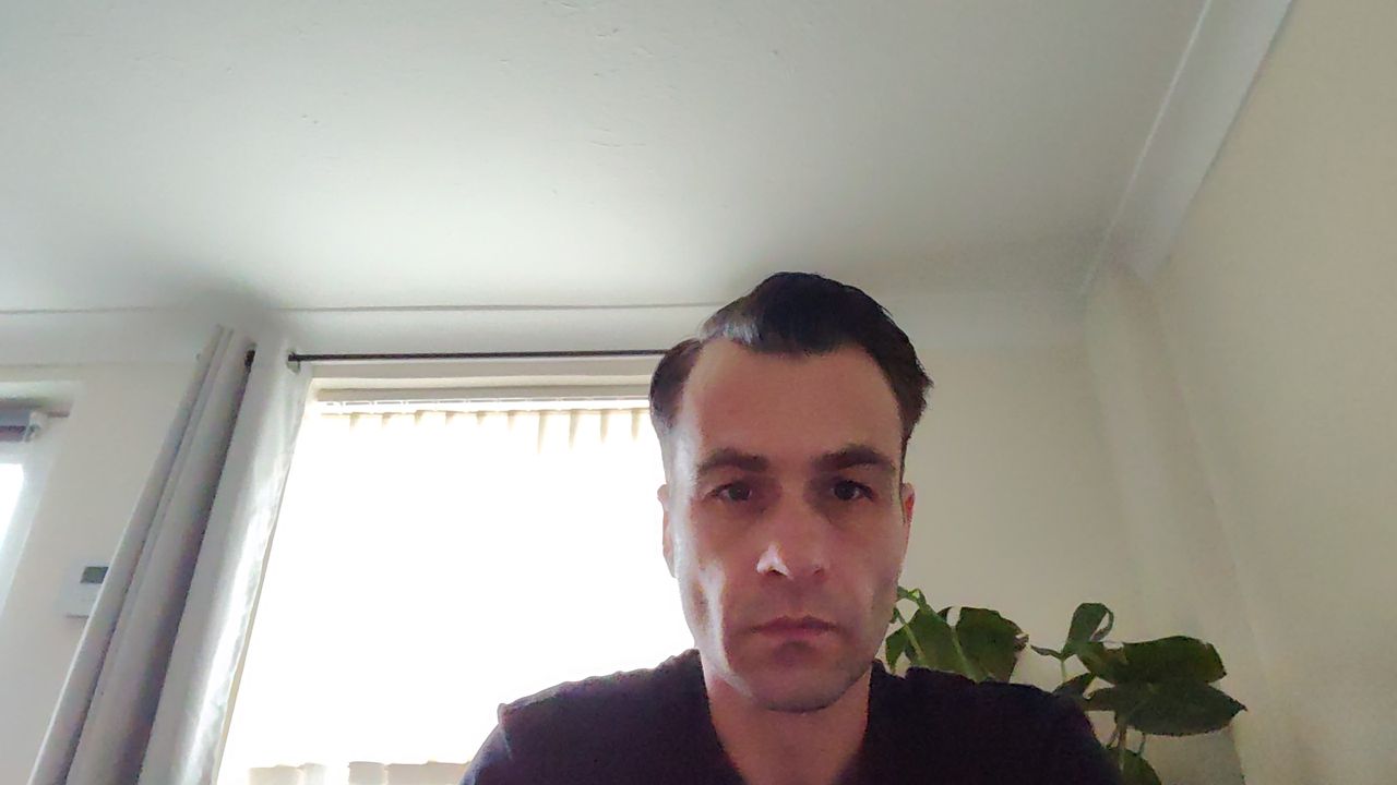 A man sitting in a room in front of a window with a plant and window behind him