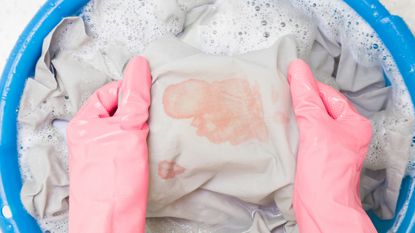 Hands in gloves handwashing a clothing item with blood stains