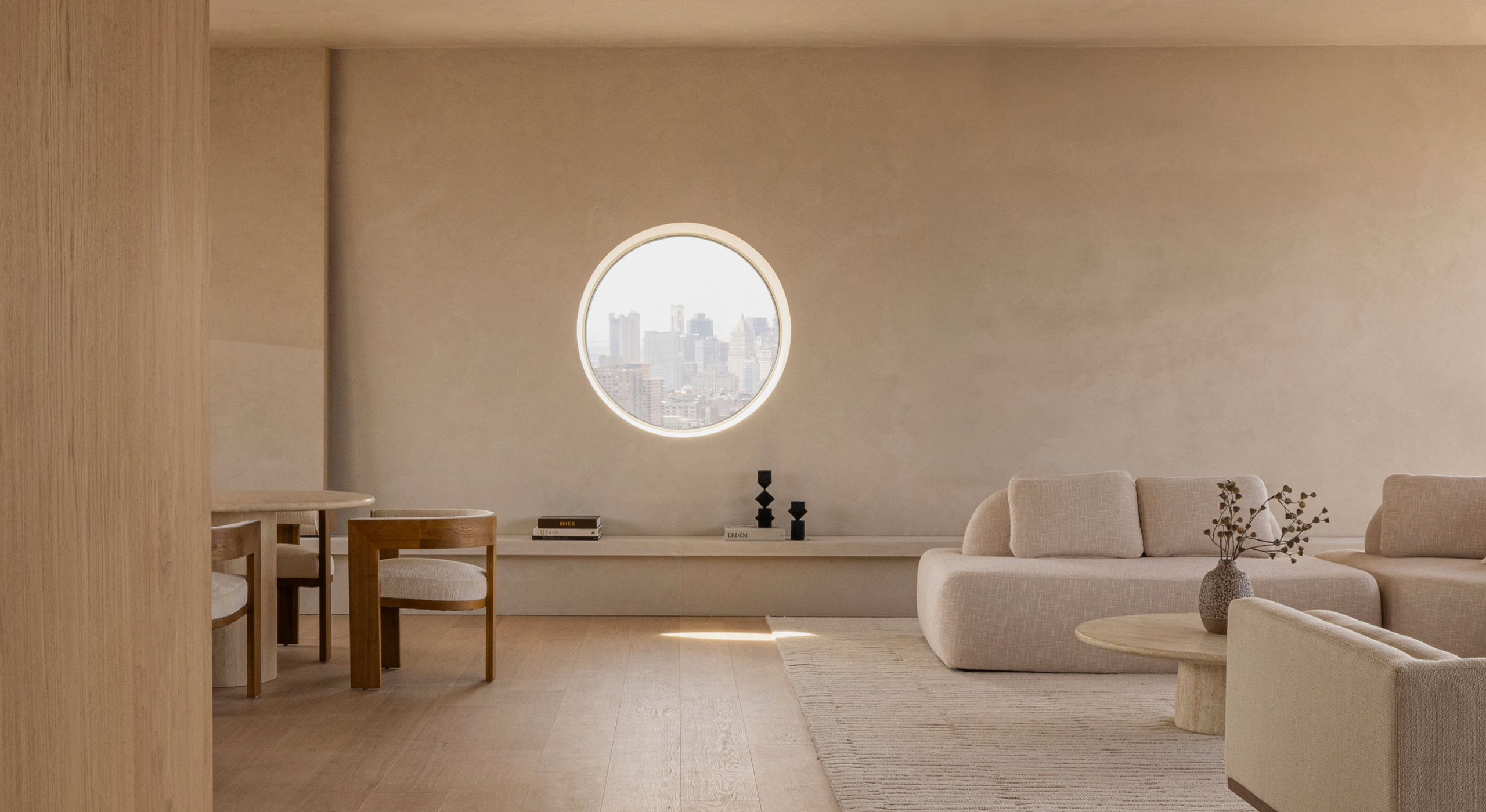 Living area at 262 Fifth Avenue by Norm Architects, with neutral-toned seating and a circular window framing a focused view of the Manhattan skyline.