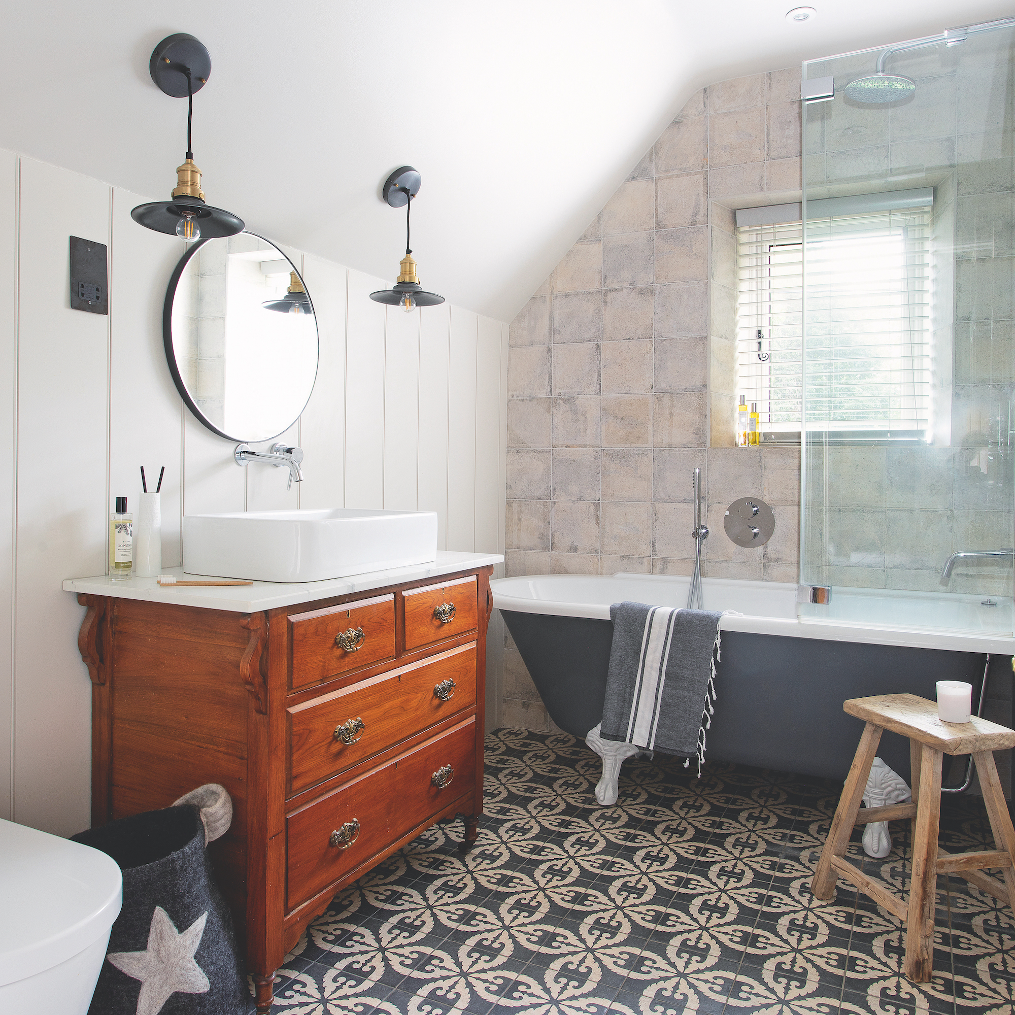 bathroom with grey patten floor tiles and grey freestanding bath with wooden dresser used as vanity with basin