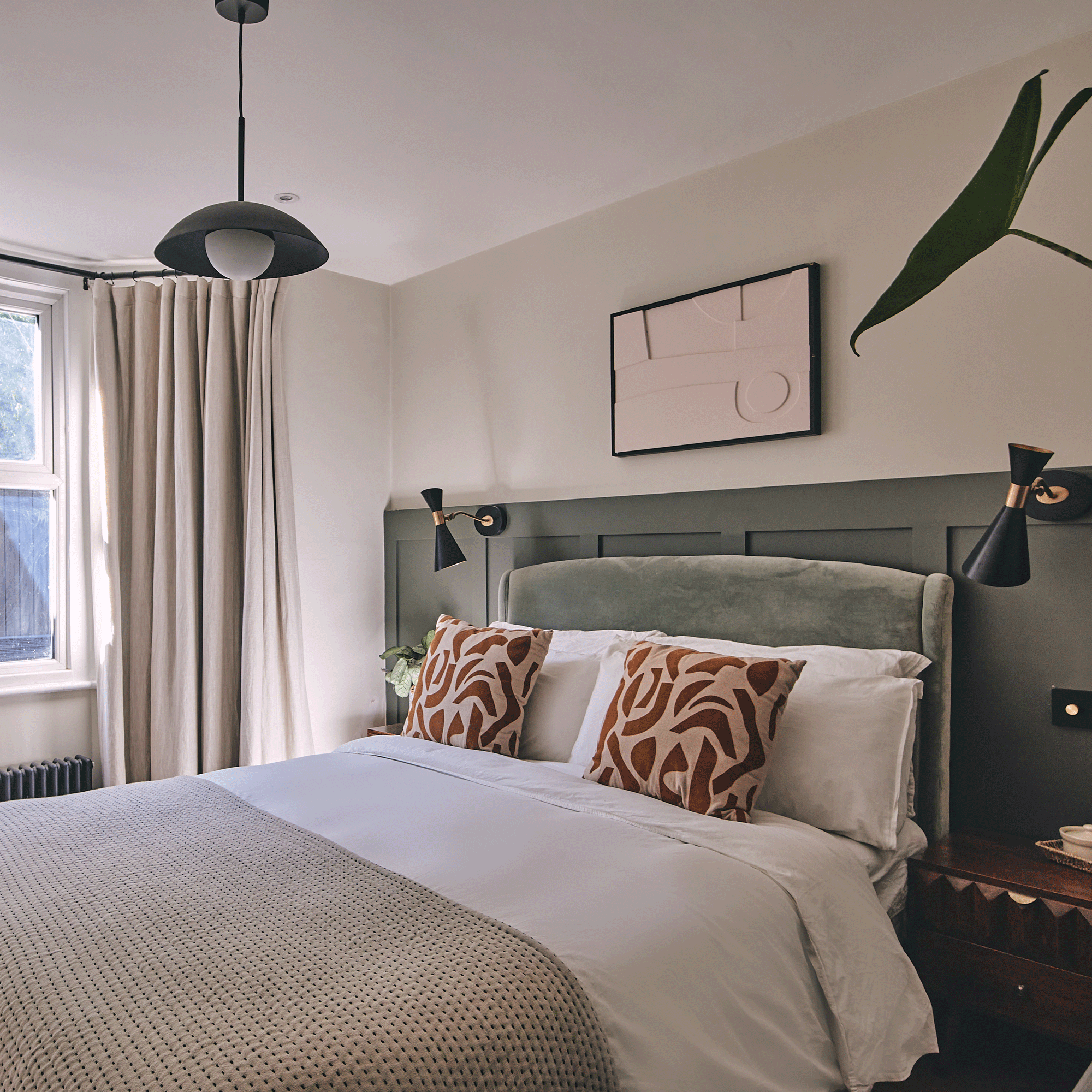 a bedroom with dark green wall panelling bedside wall lights and neutral bedding with patterned cushions