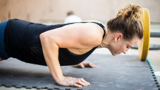 Woman performs press-up outside on mat