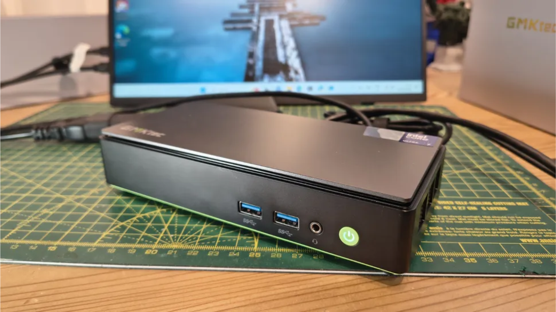 The GMKtec K13 mini PC on a desk during our testing and review process, with a monitor and the mini PC box blurred in the background