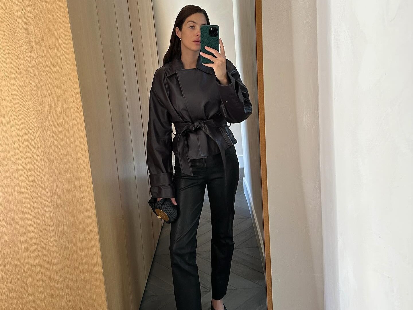 Woman wears black cigarette pants, a leather wrap coat and square toe flats.