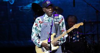 Buddy Guy onstage in dungarees playing his cream Fender Stratocaster