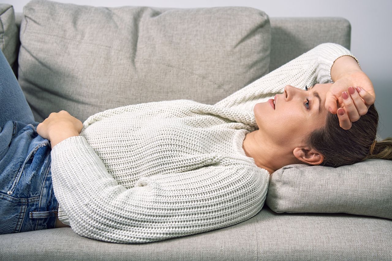 A woman lies on a sofa at home and hugs her stomach with her hands - highly sensitive person