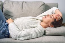 A woman lies on a sofa at home and hugs her stomach with her hands - highly sensitive person