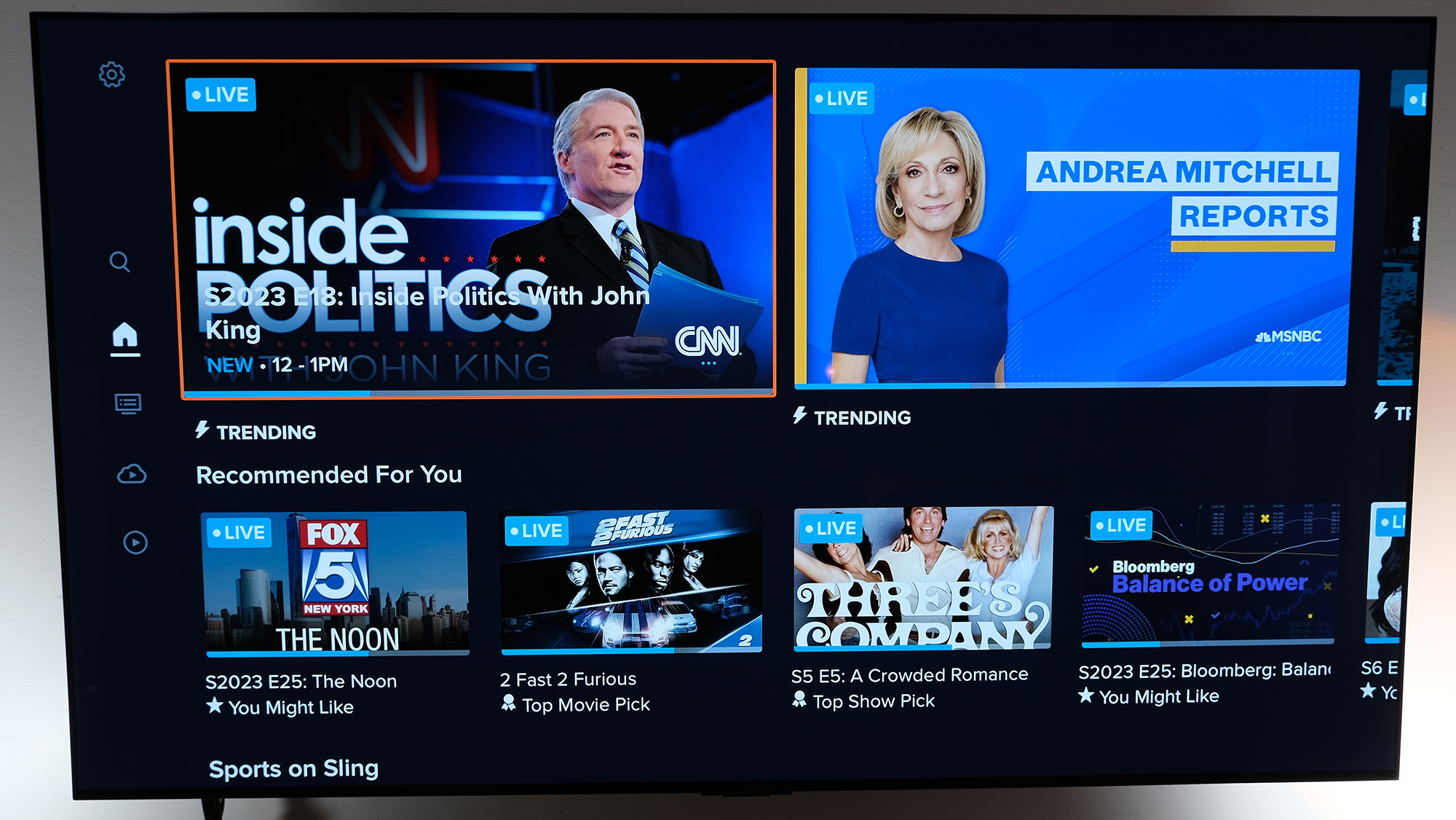 The home screen on Sling TV displays cable news options on a wall-mounted TV