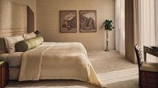 Image of all beige/off-white bedroom with carpeted floors and off-white bedding that is textured with an olive green bolster pillow.