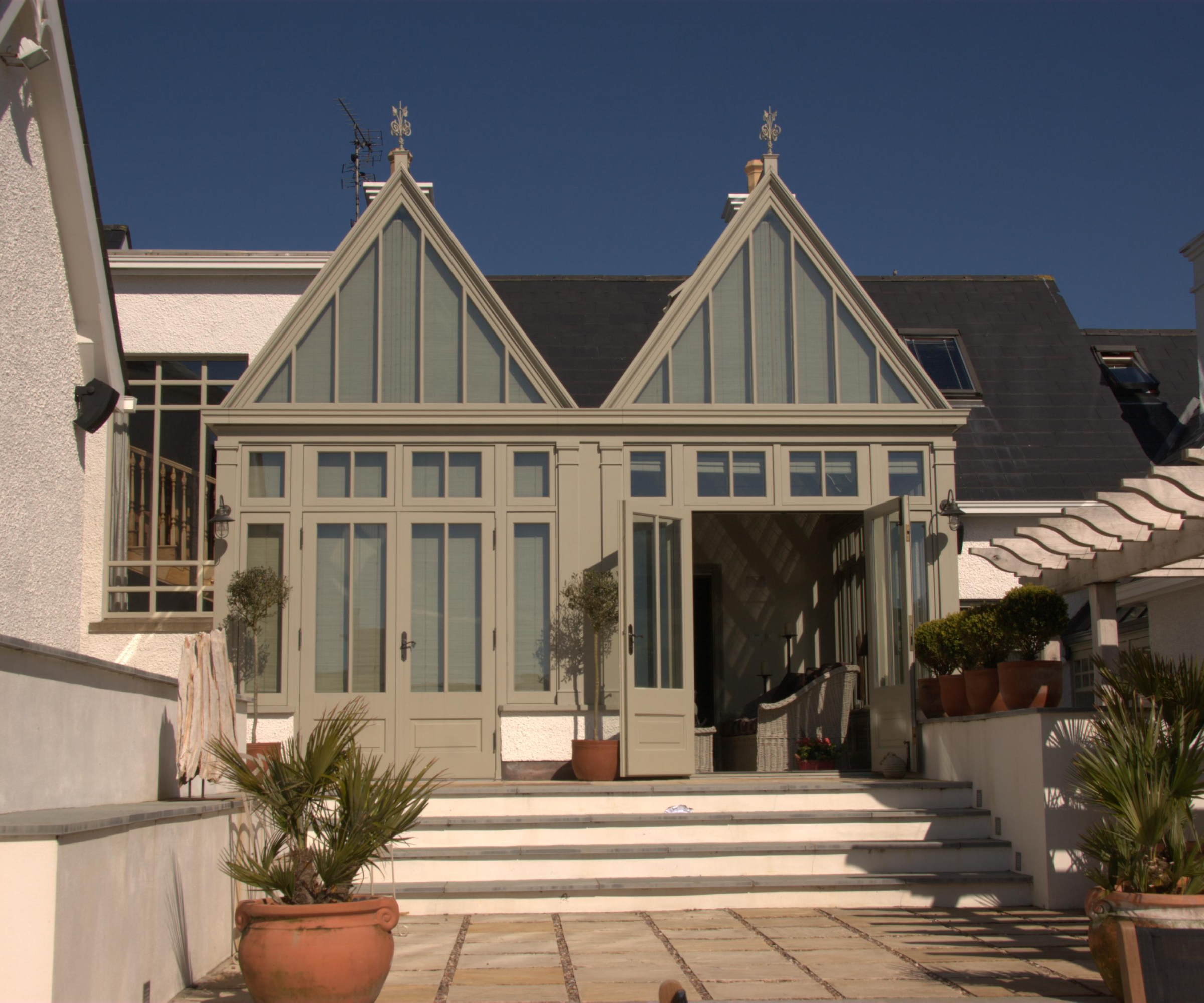 large double fronted modern conservatory with pitched roofs and gable ends in sage green