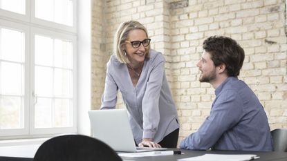 An older woman talks with a younger man in a conference room.