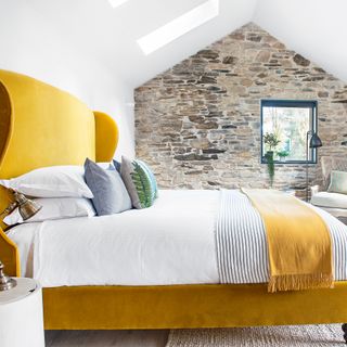 Bedroom with vaulted ceiling, skylights, exposed stone wall and ochre bed