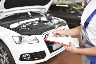 Car mechanic holding a clipboard in a garage.