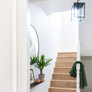 White hallway with wooden stairs and a black and glass ceiling light