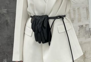 Danish fashion influencer Singe Emilie Olesen wearing black leather gloves tucked into a leather cord belt around a white blazer.