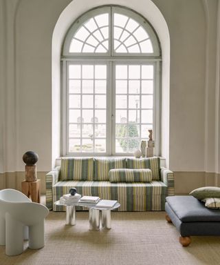 Modern living room design in traditional interior, sofa with striped upholstered covers, armchairs and lounge chairs working with sofa to create a sociable seat space, large arch window