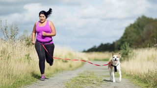 Woman running with dog on waist leash