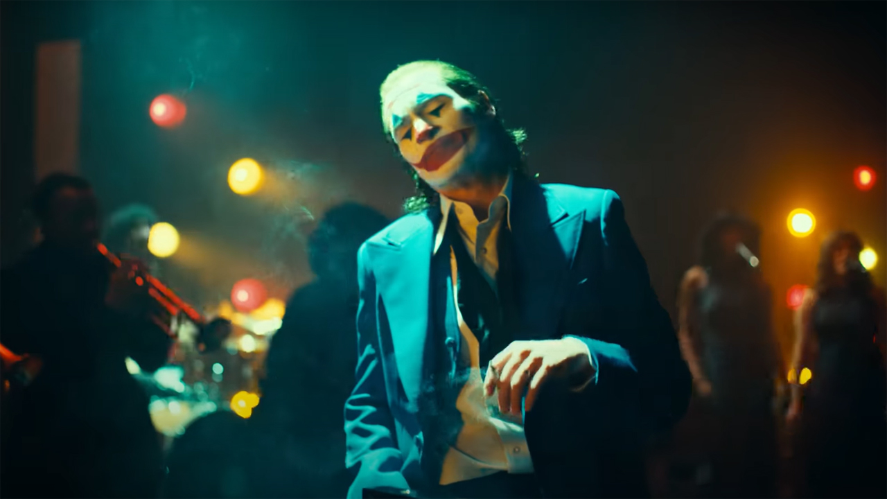 Arthur Fleck wears his signature makeup and a blue suit in a jazz club in Joker 2