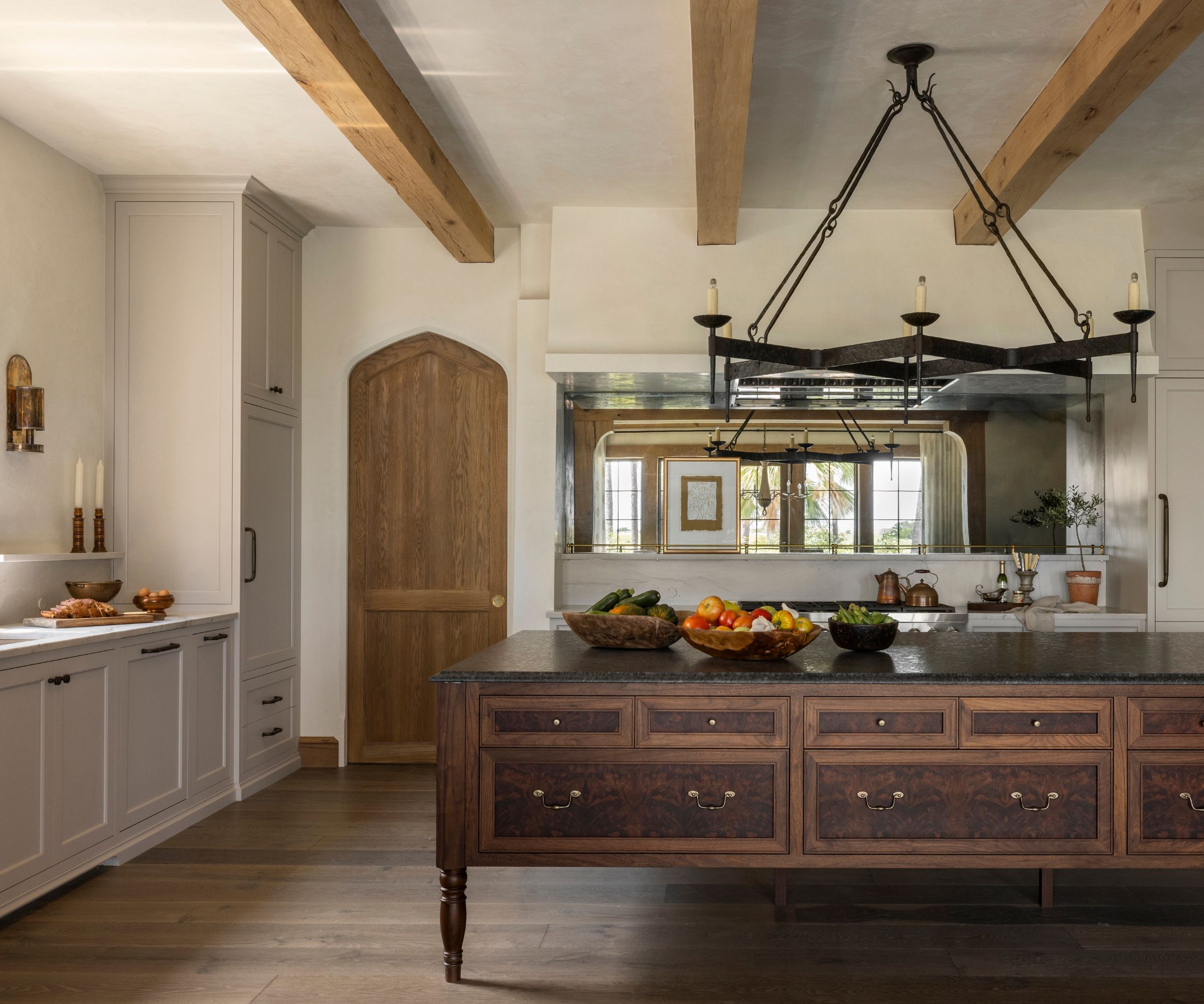 A modern rustic kitchen with a large antique wooden island, wood floors, creamy white cabinets, exposed ceiling beams, and a wooden door.