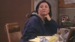 Roseanne Barr looks over wistfully while sitting at a writing desk in the Roseanne series finale.