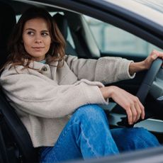 a woman in a car with one hand on the steering wheel