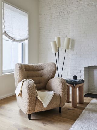 A pink/nude colored accent chair against a white painted brick wall