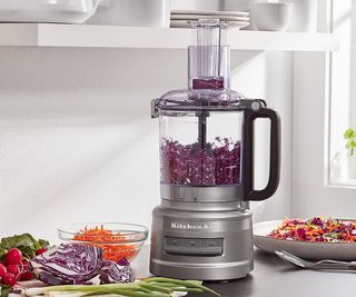 KitchenAid 9-cup food processor on a countertop with fruits and vegetables around it