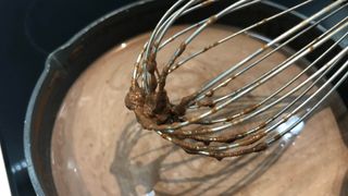 A whisk with melting chocolate on the end above hot chocolate