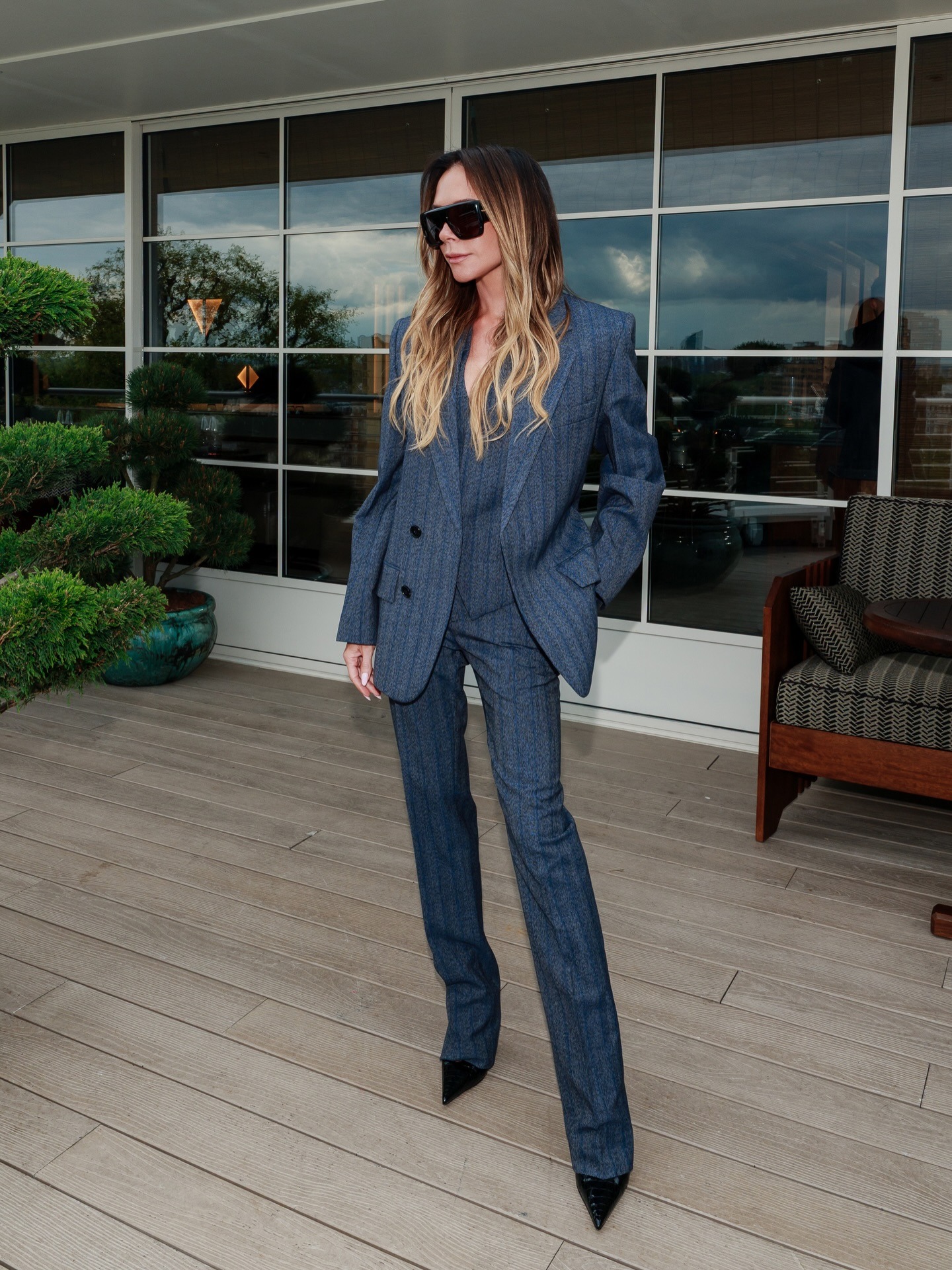 Victoria Beckham wears a striped suit with patent leather croc print heels and oversized sunglasses.