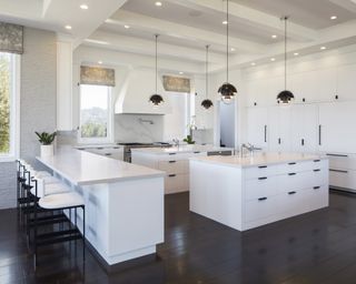 A kitchen lighting idea with downlighters and black pendany lights over pair of white islands