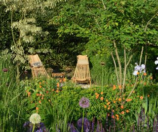 A small outdoor seating area completely surrounded with flowers and small specimen trees